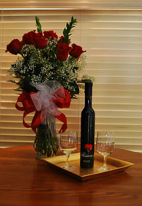 View of bottle of wine and glasses next to vase of bright red roses.