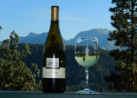 Exterior view of wine bottle and glass of wine set against blue mountains in background.