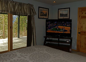 Interior view of room showing large HDTV, bed and sliding glass doors with view of mountains.