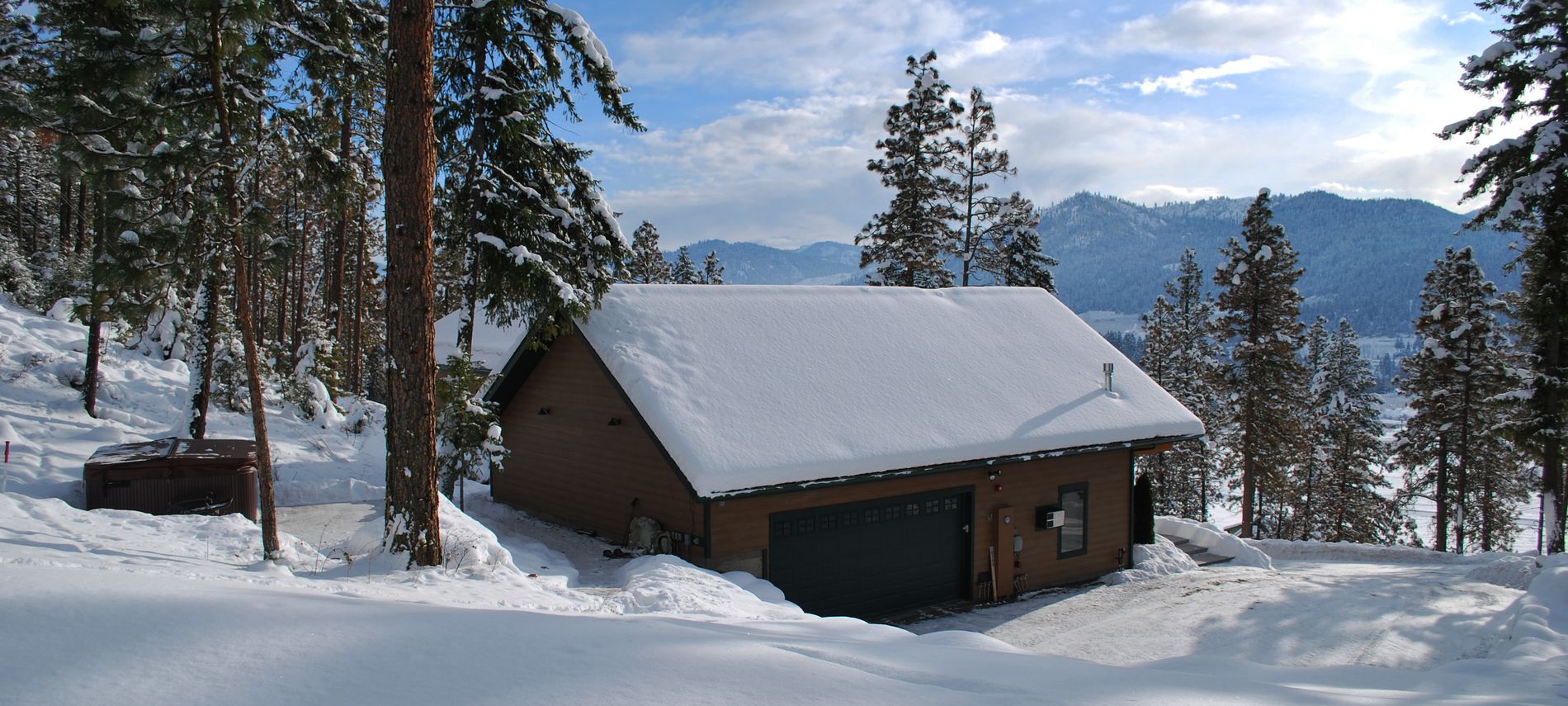 Exterior winter view of outdoor hot tub surrounded by white snow and dark blue mountains in the distance.