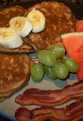 View of breakfast dish showing yellow bananas, red watermelon and green grapes.